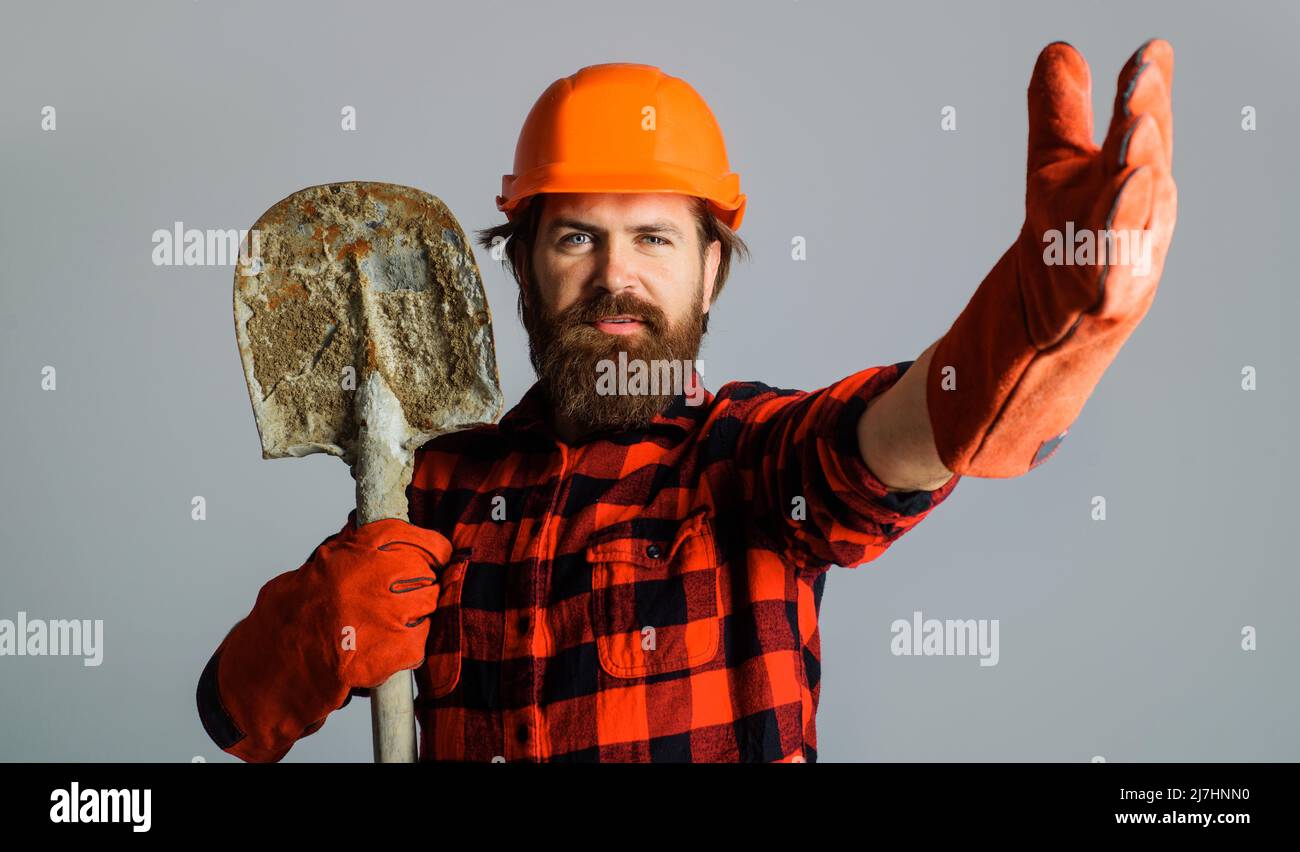 Costruttore in casco protettivo e guanti da lavoro con pala. Uomo da lavoro con bearded in elmetto con lancetta. Foto Stock