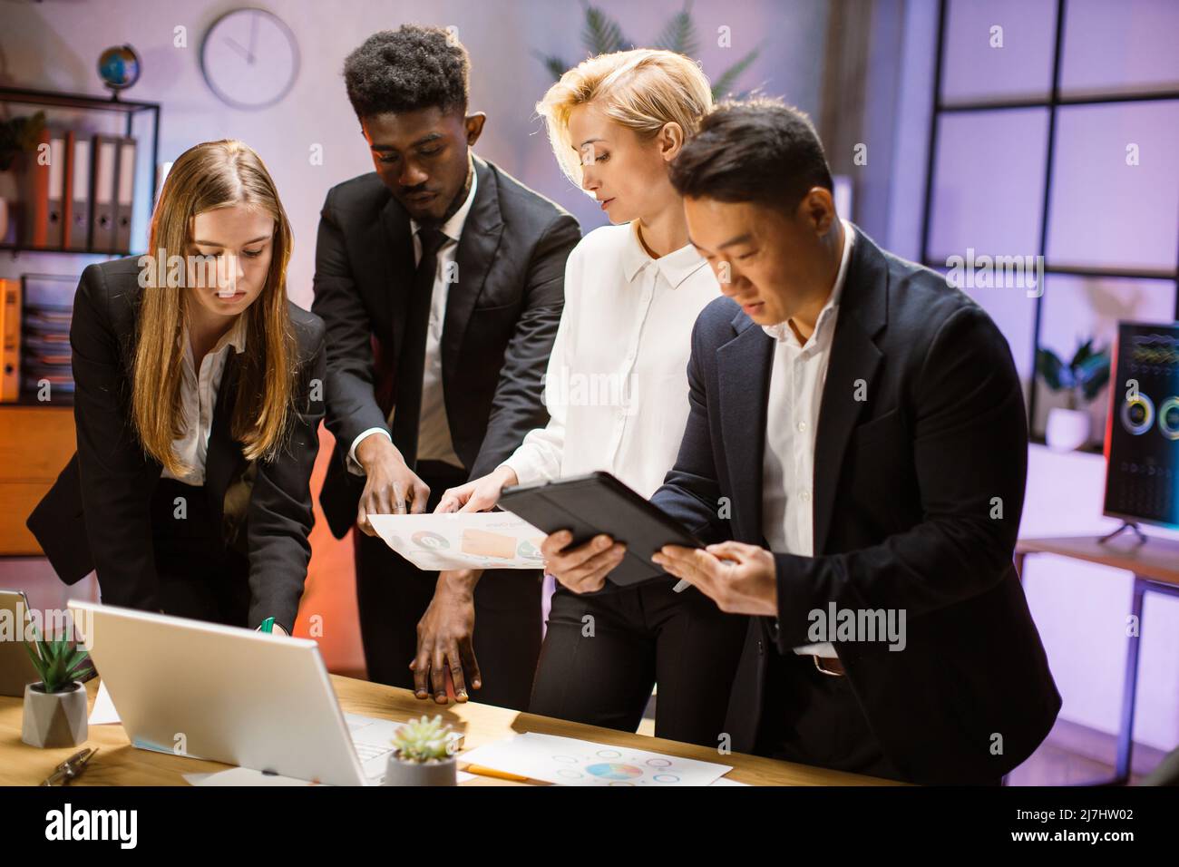 Gruppo multietnico di quattro persone motivate che lavorano insieme a un nuovo progetto, utilizzando gadget e report, condividendo idee creative. Concetto di lavoro di squadra e cooperazione Foto Stock