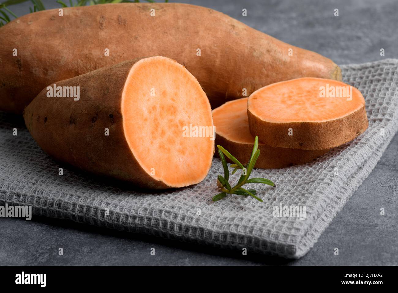 Patate dolci crude e arancioni intere e fette di batata con rosmarino fresco su sfondo di cemento grigio, vista dall'alto, spazio copia, giacitura piatta Foto Stock