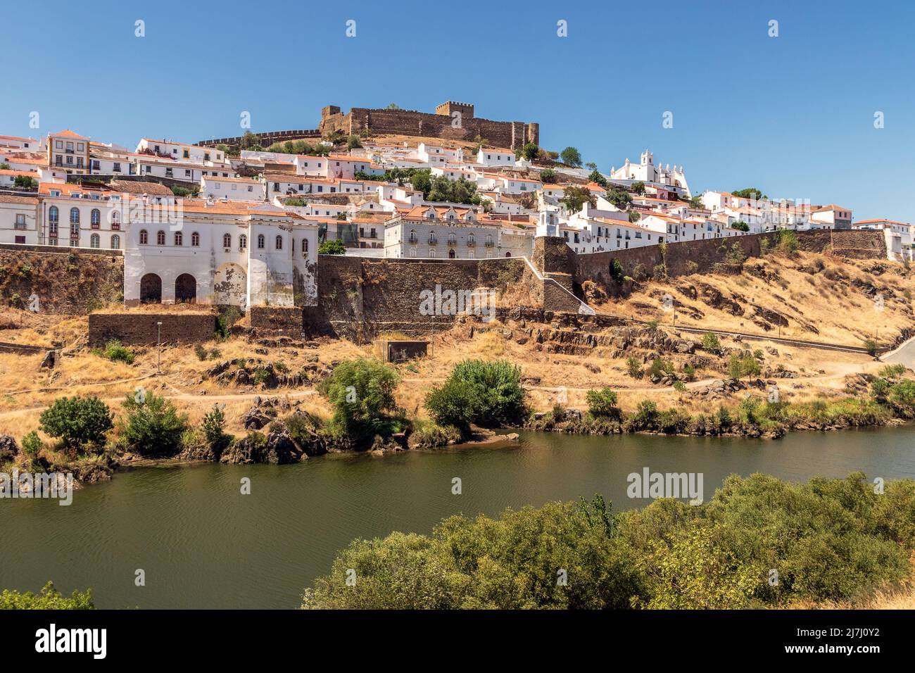 Vista sul villaggio di Mértola in Portogallo, con il fiume Guadiana in primo piano, in una giornata di sole in estate. Foto Stock