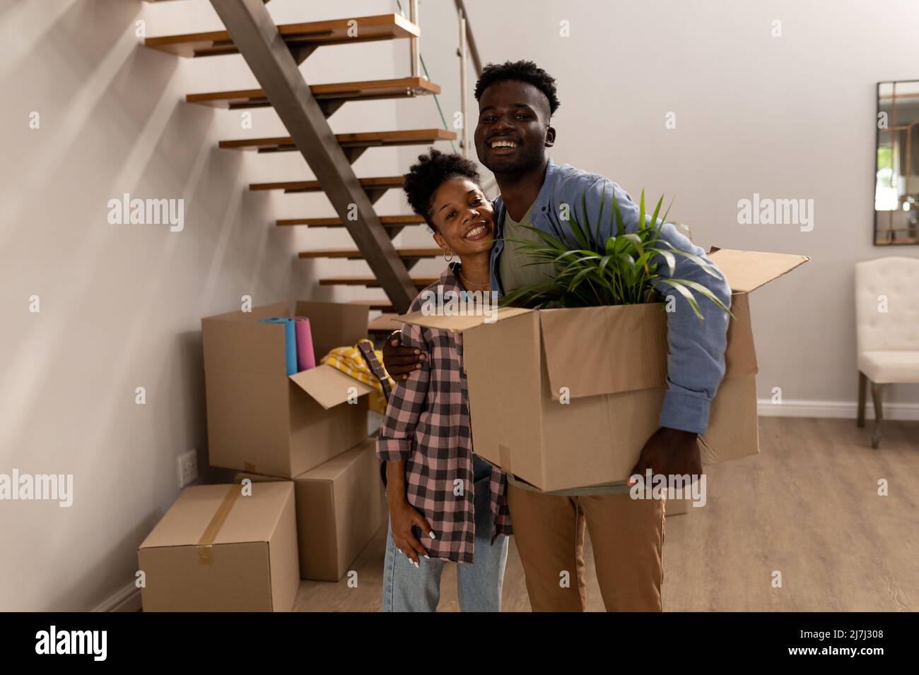 Ritratto di felice afroamericano giovane uomo che porta scatola di cartone e ragazza abbracciante a casa Foto Stock