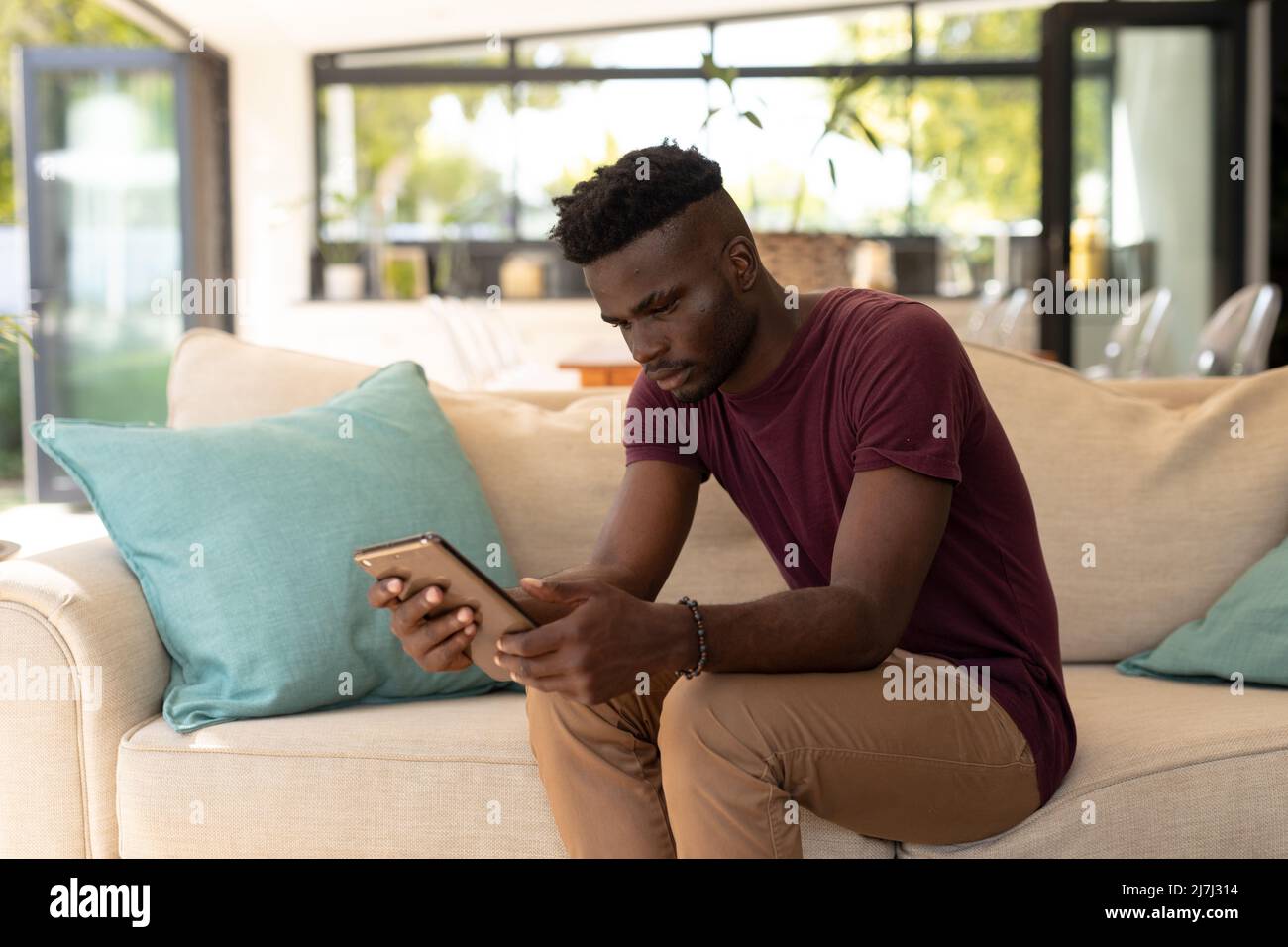 Il giovane afro-americano usa un tablet digitale mentre si siede sul divano nel soggiorno di casa Foto Stock