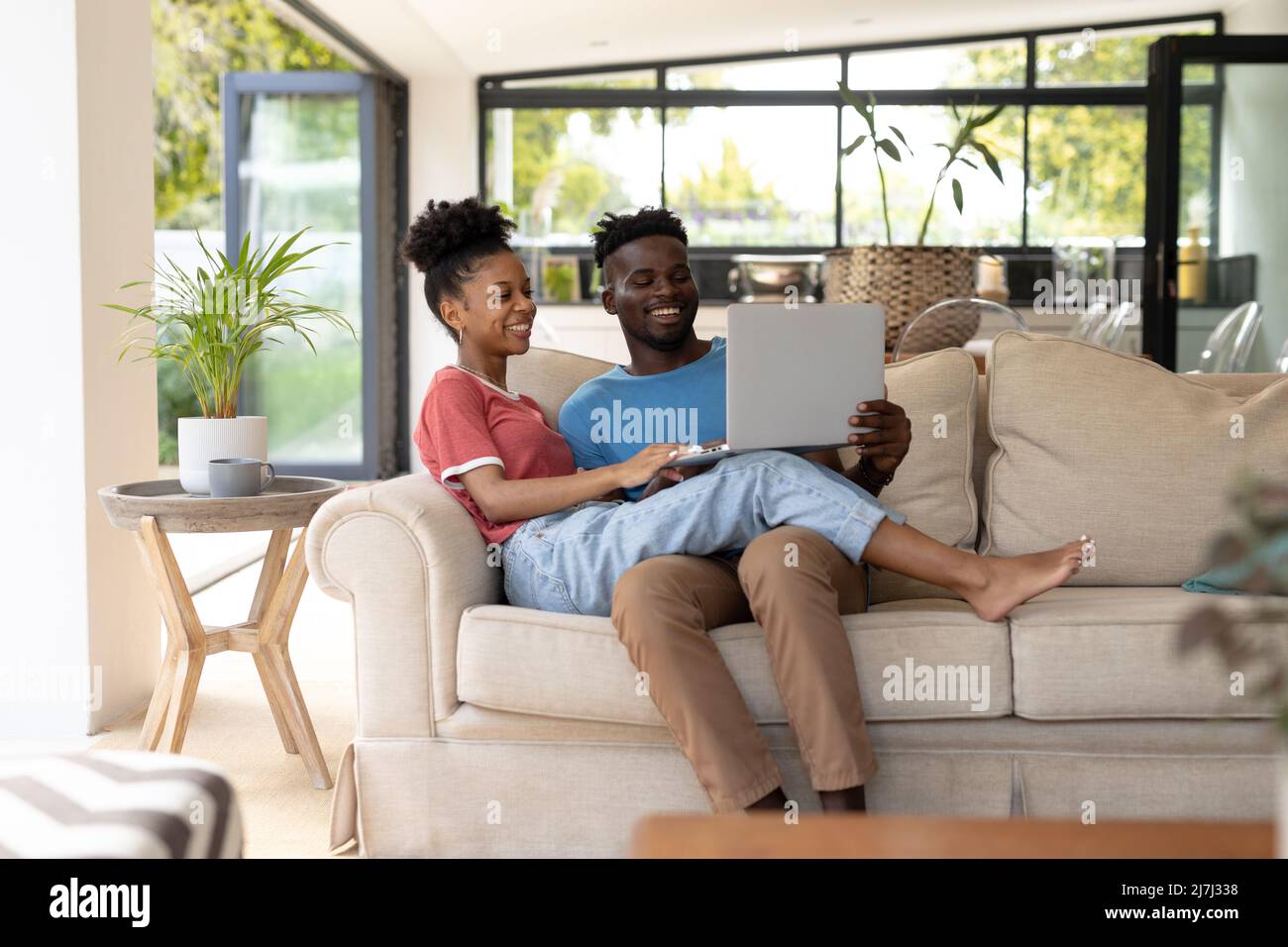 Allegra giovane coppia afroamericana che usa un computer portatile mentre si siede sul divano nel soggiorno di casa Foto Stock