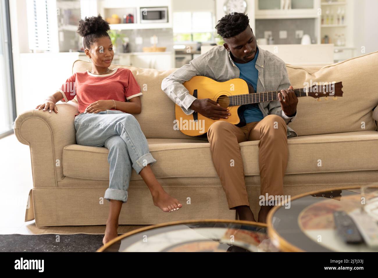 Sorridente giovane afroamericana che guarda il ragazzo suonare la chitarra sul divano in salotto Foto Stock