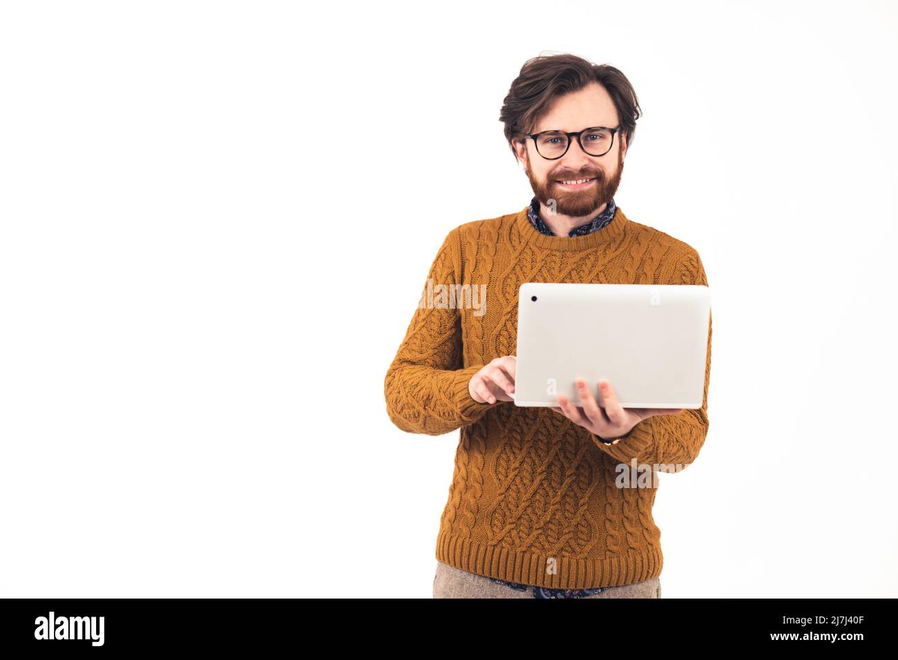 Soddisfatto buon-osservante uomo europeo gioioso nel suo 30s che indossa un maglione modellato che tiene un portatile bianco, guardando la macchina fotografica. Foto di alta qualità Foto Stock