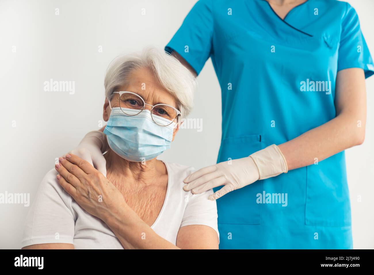 Sottile non riconoscibile medico specialista femminile che sostiene e tenendo una vecchia donna con capelli grigi indossando una maschera e occhiali. Foto di alta qualità Foto Stock