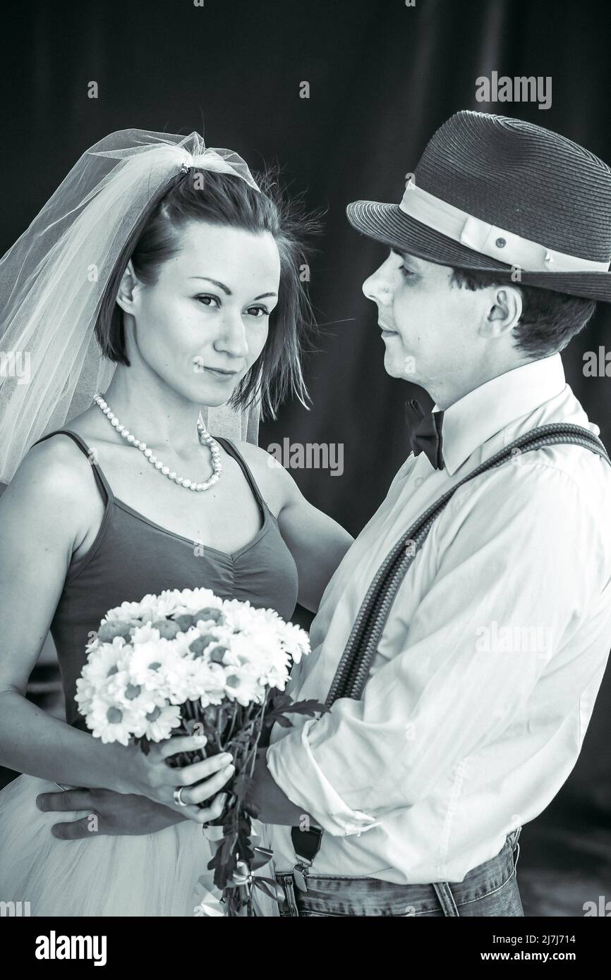 Ritratto di una giovane coppia in abito da sposa che celebra il loro anniversario di matrimonio in bianco e nero. Sorridi, bacia, tenendo insieme il bouquet, amore Foto Stock
