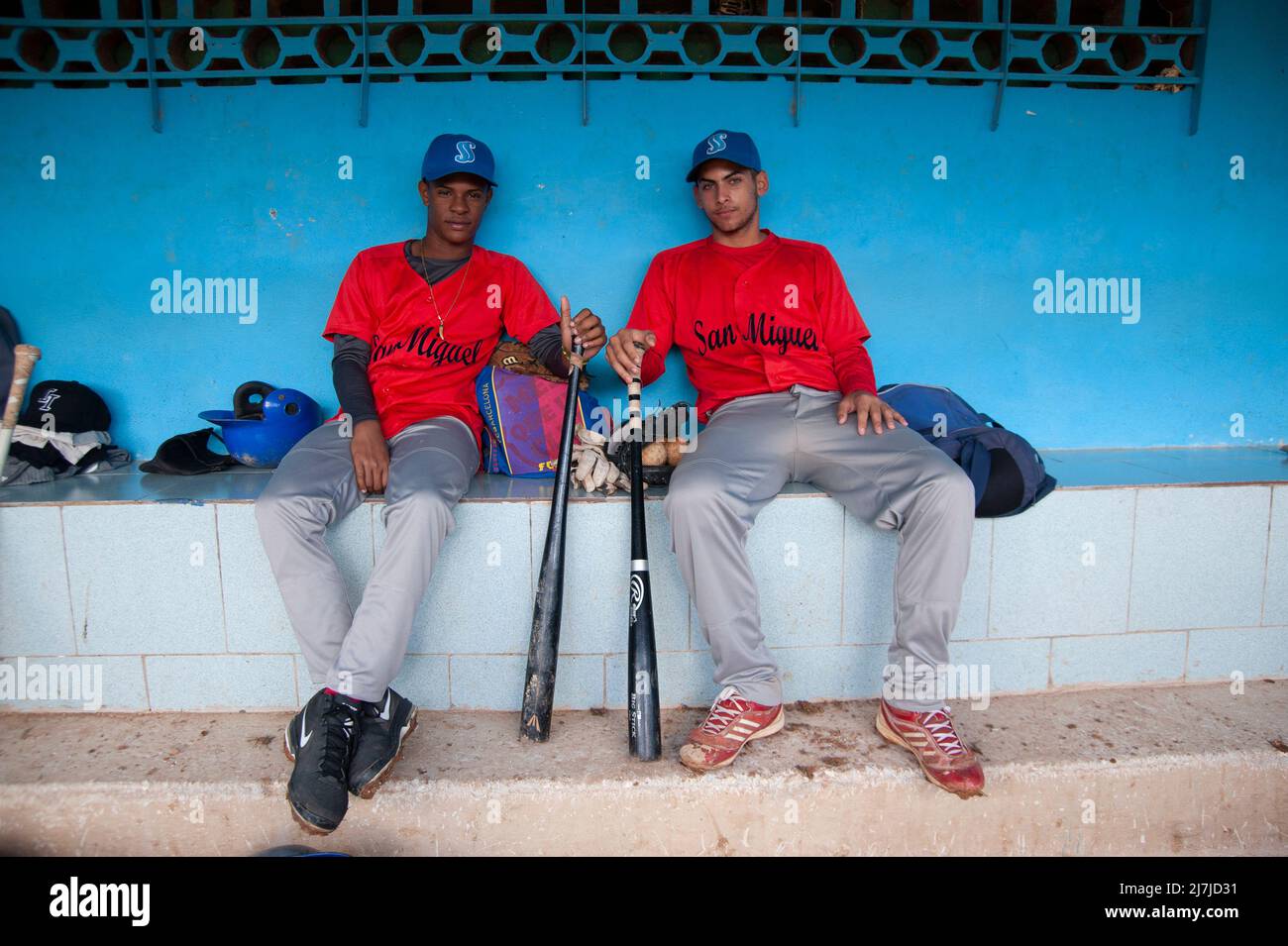 I giocatori cubani di baseball seduti nel dugout tenendo le loro mazze da baseball. Foto Stock