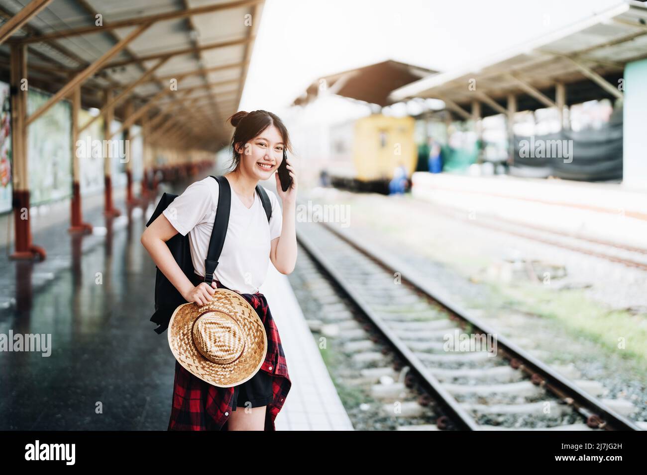 Estate, relax, vacanza, viaggio, ritratto di bella ragazza asiatica utilizzando lo smartphone cellulare per chiamare gli amici alla stazione ferroviaria mentre si aspetta Foto Stock