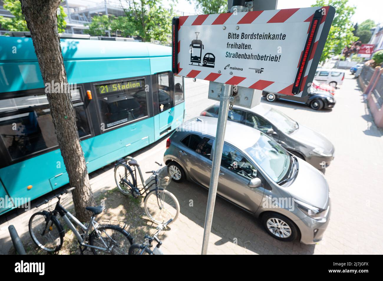 09 maggio 2022, Hessen, Francoforte sul meno: Un tram passa davanti a un'auto parcheggiata appena fuori dai binari di Schwarzwaldstraße. In primo piano è appeso un cartello con le luci che indica 'tenere il marciapiede a distanza. Funzionamento del veicolo stradale." C'è un progetto pilota in strada che utilizza sensori a terra per avvisare gli automobilisti quando sono parcheggiati troppo vicino ai binari. (A dpa 'Falso parker ostacolano autobus e treni - il progetto pilota a Francoforte continua') Foto: Sebastian Gollnow/dpa Foto Stock