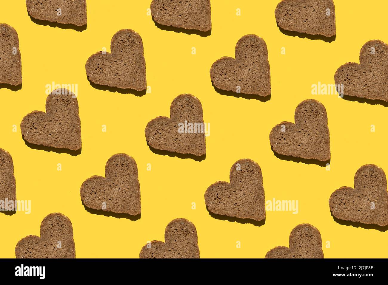 Modello fatto con pane a forma di cuore su sfondo giallo, come sfondo o texture. Carta da parati alimentare luminosa. Vista dall'alto, disposizione piatta. Foto Stock