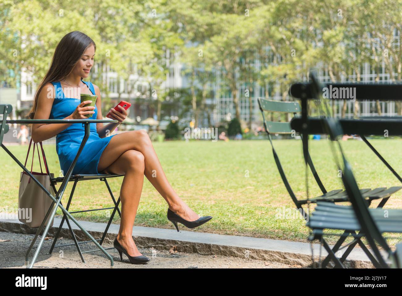 New York City Life. Multiculturale giovane professionista bere succo di frullato verde utilizzando l'app per telefono a Bryant Park, Manhattan. Foto Stock