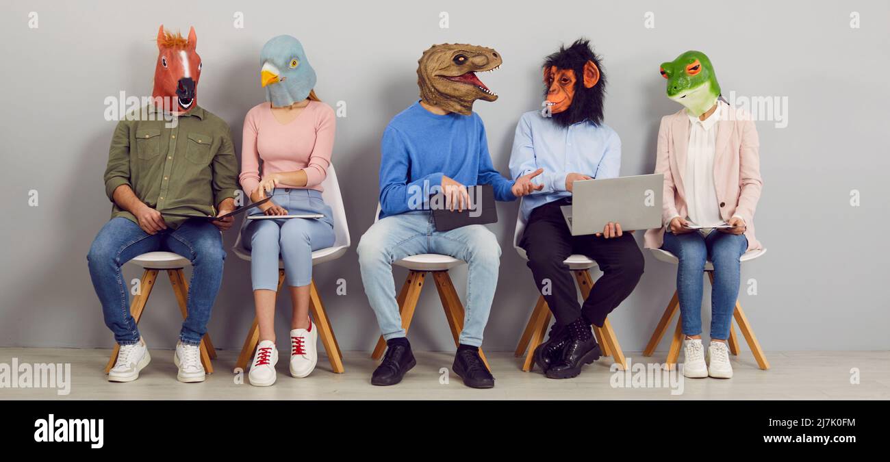 Persone divertenti che indossano maschere animali seduti in sala d'attesa, utilizzando computer portatili e parlando Foto Stock