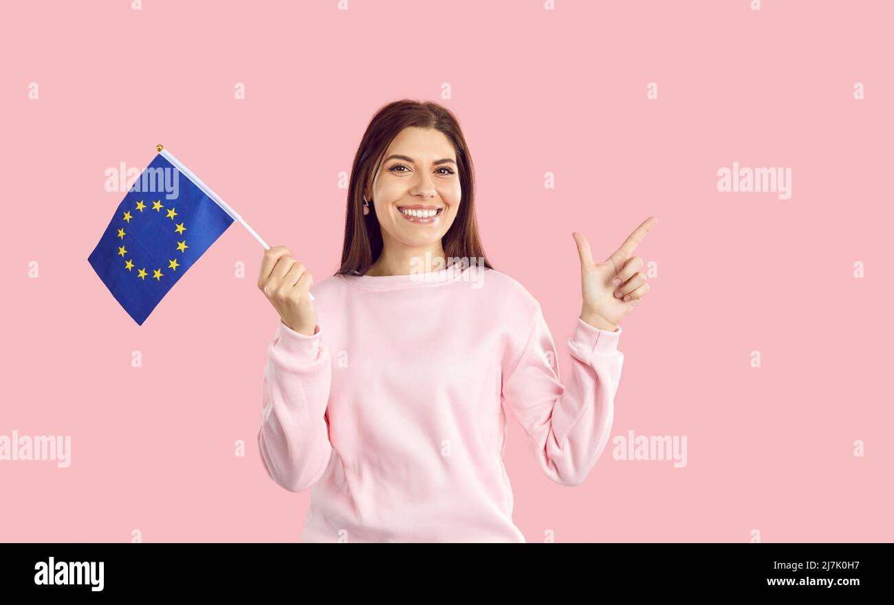 Donna caucasica con bandiera piccola con emblema dell'Unione europea isolato su sfondo rosa. Foto Stock