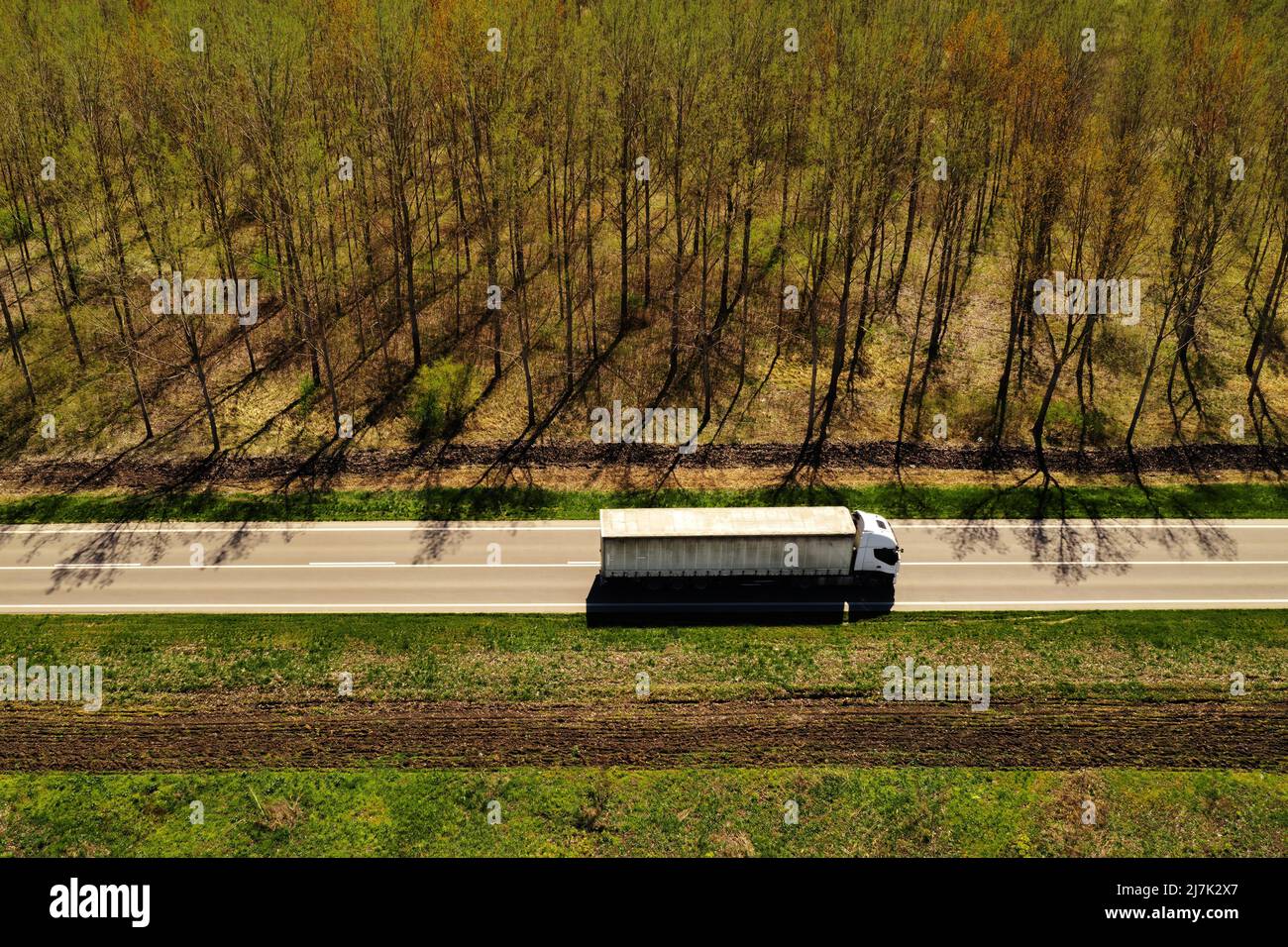 Scatto aereo con vista ad angolo alto del semi-camion su autostrada con paesaggio boscoso sullo sfondo, concetto di industria dei trasporti Foto Stock