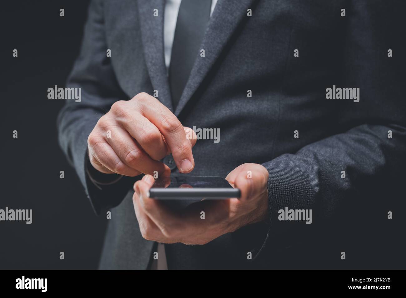 Elegante uomo d'affari in grigio scuro vestito sta usando il telefono cellulare smart, primo piano della mano digitando il messaggio di testo, fuoco selettivo Foto Stock