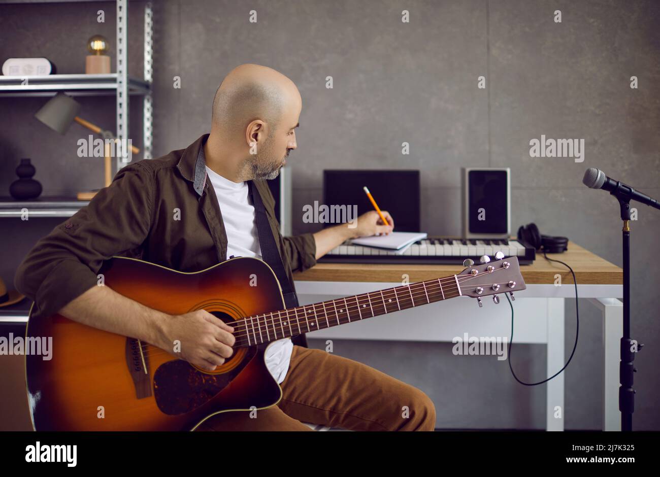 Un compositore di musica maschile di talento scrive testi e note in un notebook mentre suona la chitarra. Foto Stock