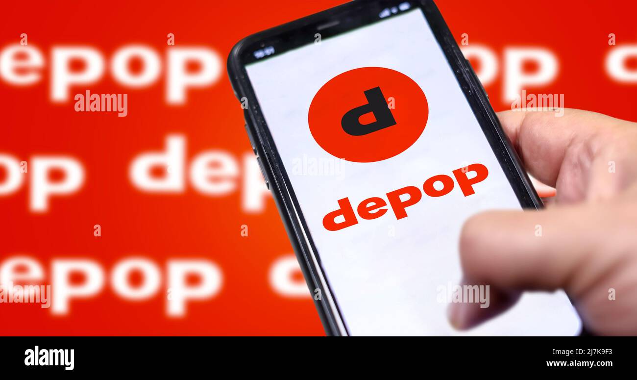 Roncade, Italy, May 2022: Mano maschile che tiene un telefono con Depop pagina web aziendale sullo schermo. Sullo sfondo il logo Deppop sfocò e ripeté. Dopo Foto Stock