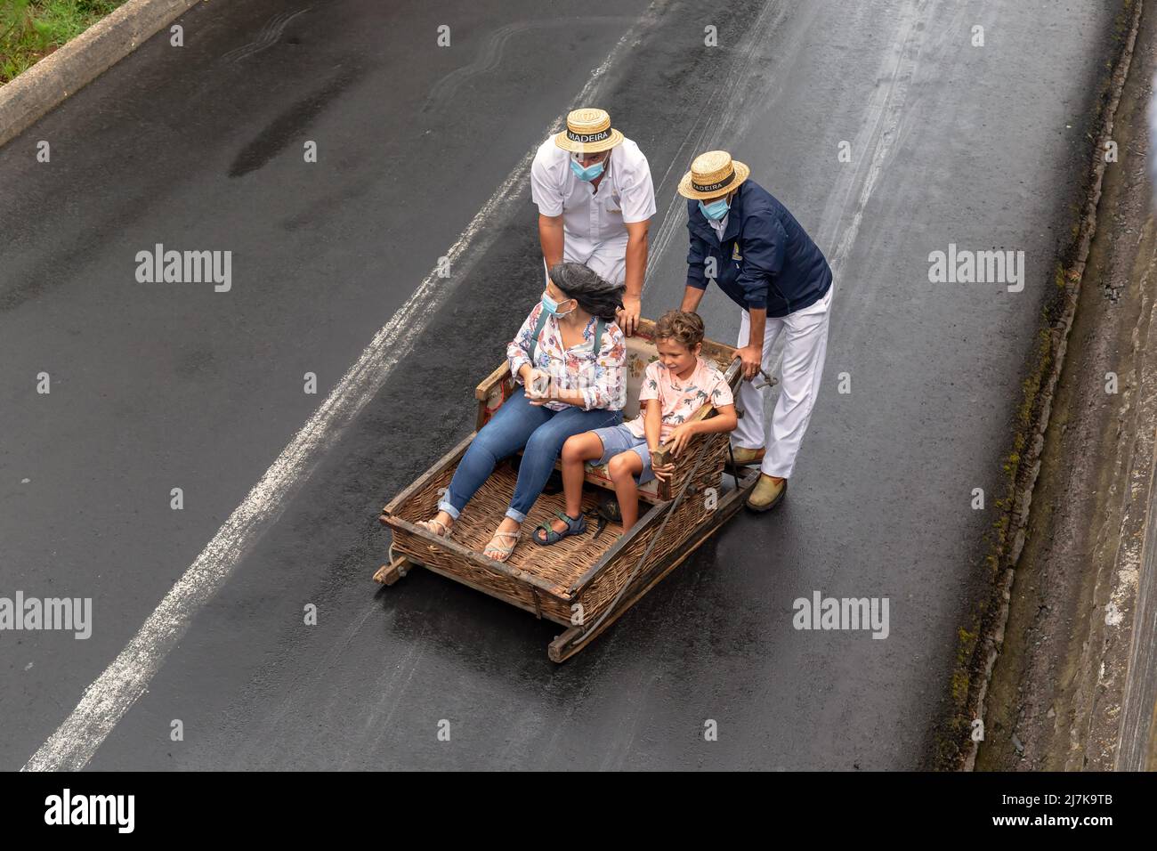 FUNCHAL, PORTOGALLO - 24 AGOSTO 2021: Donna e bambino non identificati rotolare giù per la strada in cesti di vimini (toboga) con l'aiuto dei conducenti. Foto Stock
