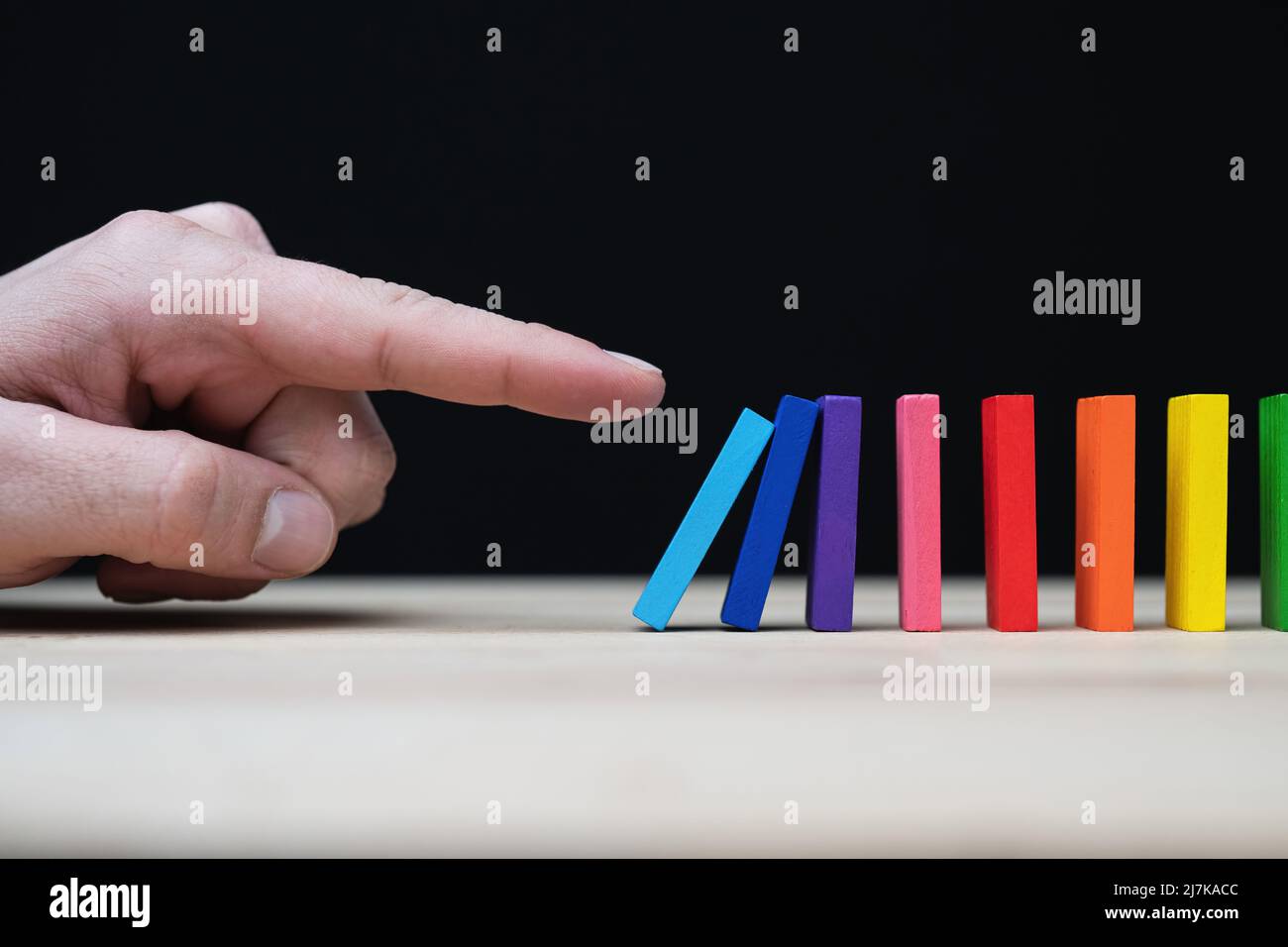 Foto concettuale di una mano che inizia una reazione a catena con dominazioni colorate. Effetto domino con pietre colorate e copyspace. Foto Stock