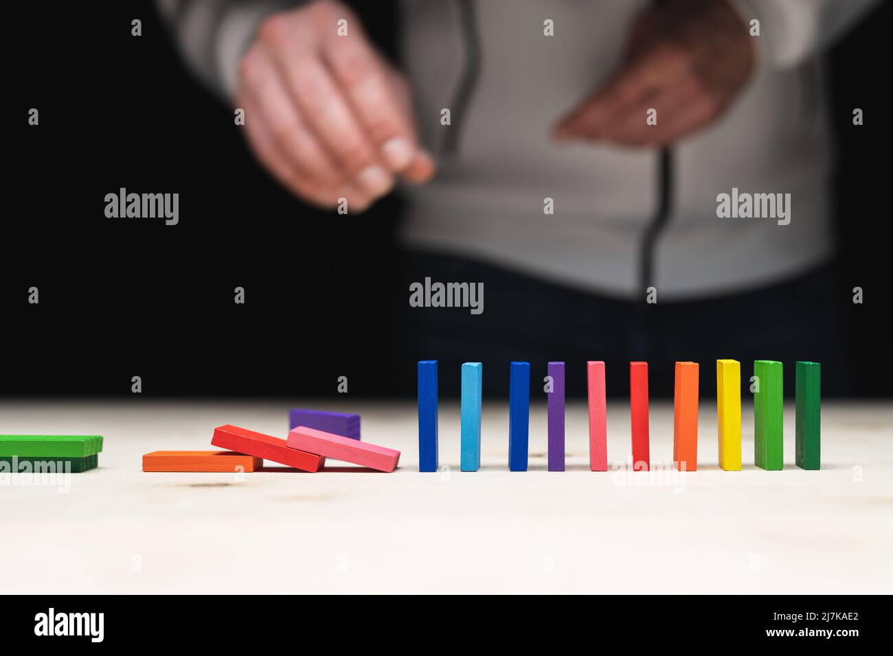 Foto concettuale di una mano che mette una pietra ad una fila di pietre domino. Effetto domino con pietre colorate e copyspace Foto Stock