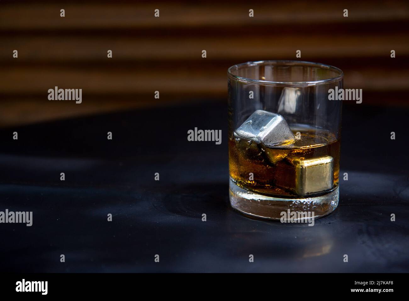 Bicchiere di whiskey e cubetti di ghiaccio in metallo sul tavolo Foto Stock