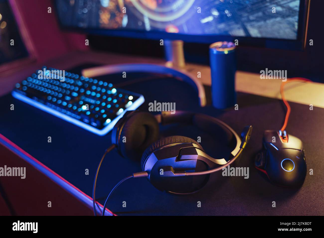 Vista della configurazione professionale della scrivania da gioco con cuffia, tastiera, monitor e mouse illuminati da luci al neon. Le attrezzature per Cyber sport si poggiano su un desktop e sono pronte per lo streaming e i giochi online di sparatutto video Foto Stock