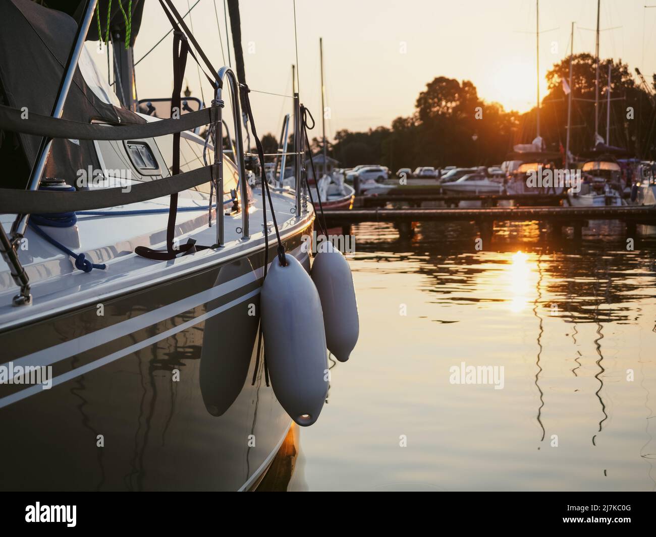 vista del tramonto sullo yacht ormeggiato sul molo nel porto, vista ravvicinata sullo scafo della barca a vela, la prua e i parafanghi Foto Stock