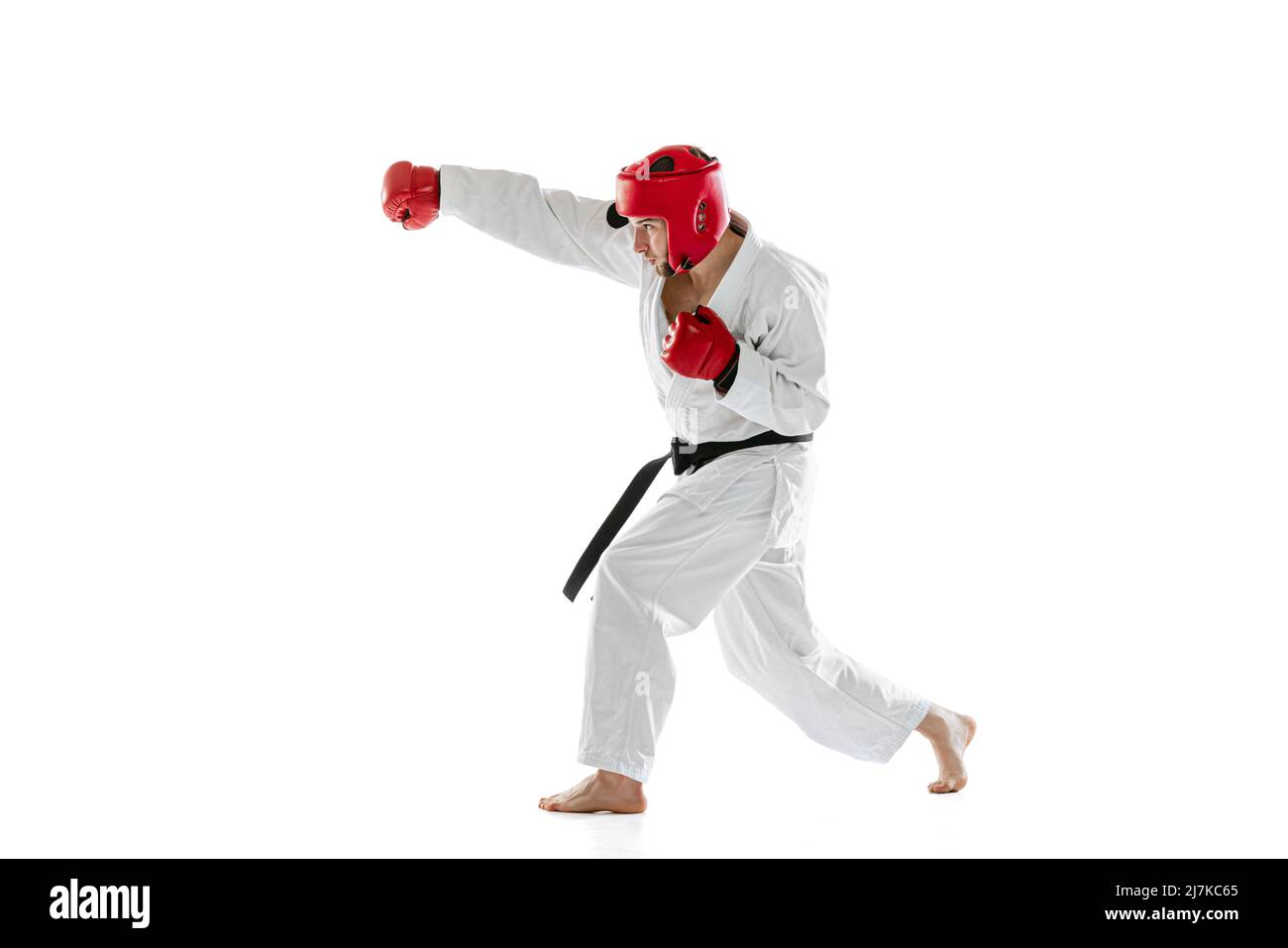 Ritratto di giovane sportivo indossando il dobok bianco, casco e guanti che praticano isolato su sfondo bianco. Concetto di sport, allenamento, salute. Foto Stock