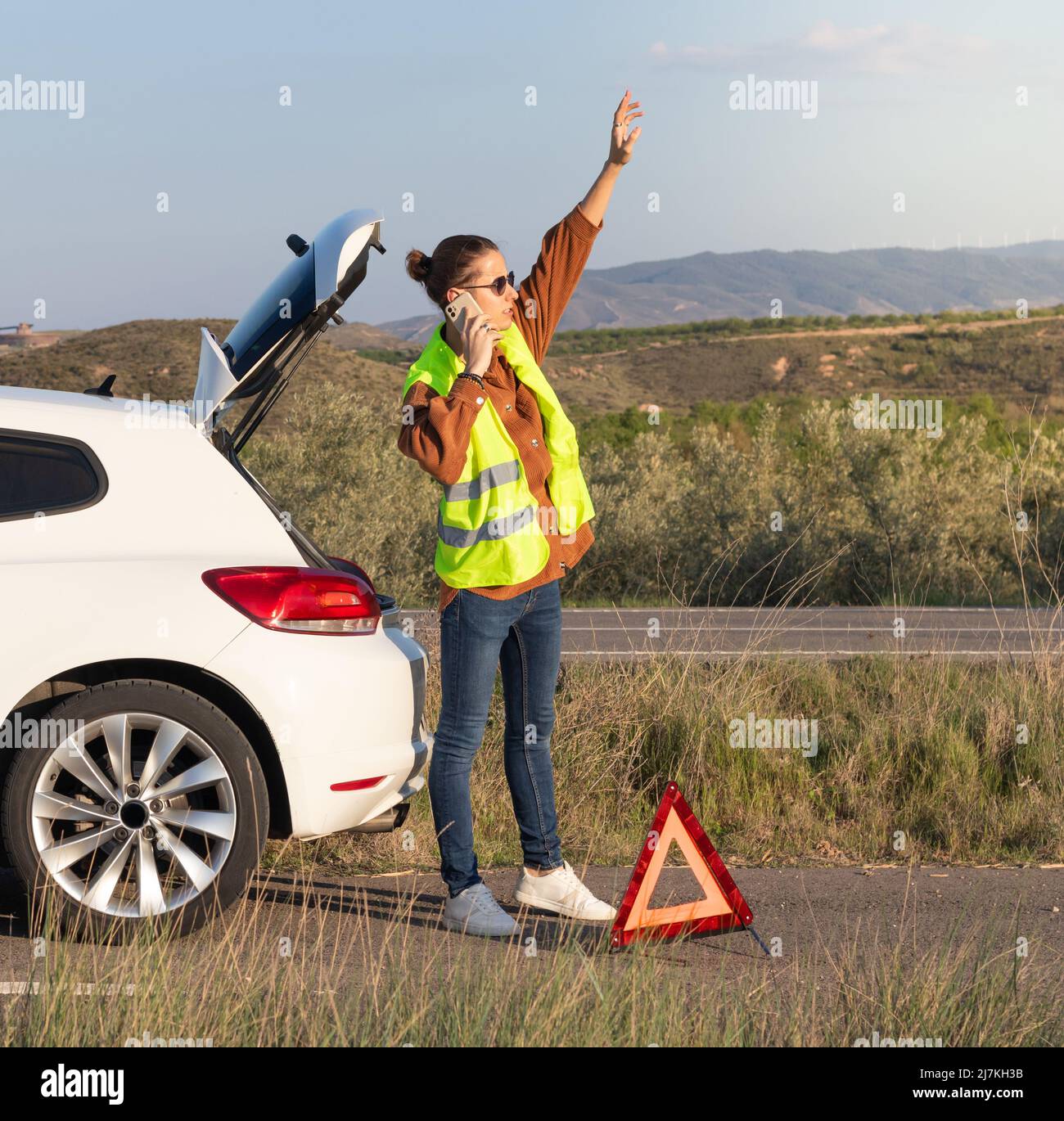 Giovane uomo su un bun che chiama assicurazione auto al telefono per aiutarlo. Sollevando il braccio in modo che l'assistente possa vederlo sulla strada Foto Stock