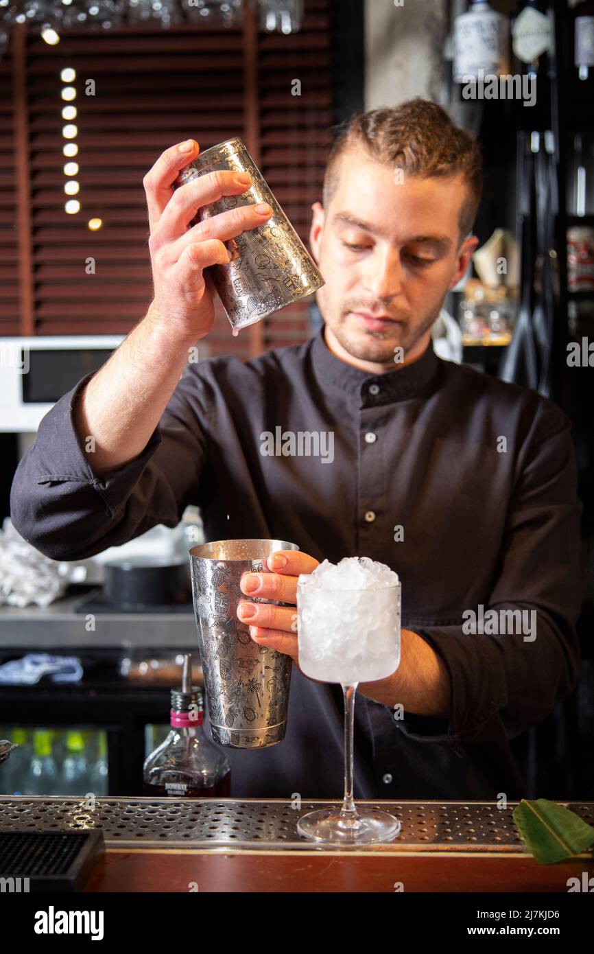 Concentrato giovane ed elegante barman maschile che mescola ingredienti in shaker mentre prepara deliziosi cocktail rinfrescanti in un ristorante contemporaneo Foto Stock