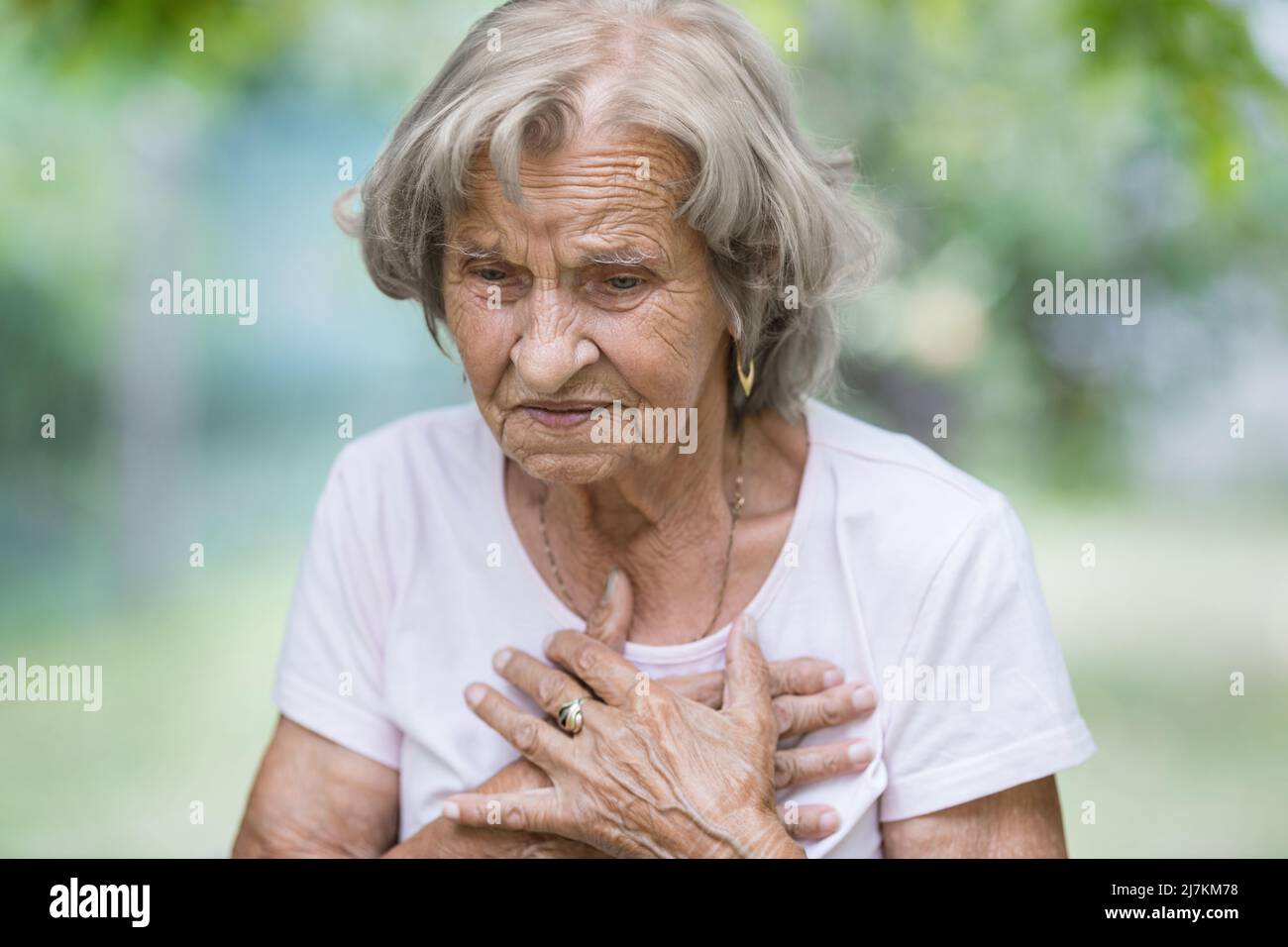 Donna anziana all'aperto con dolore al cuore che tiene il suo petto Foto Stock