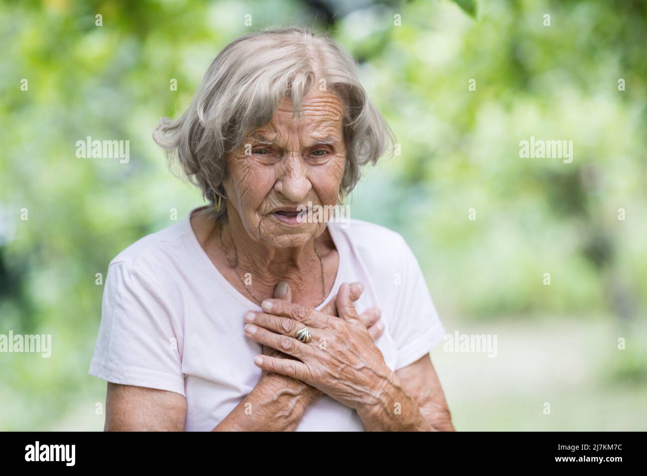 Donna anziana all'aperto con dolore al cuore che tiene il suo petto Foto Stock