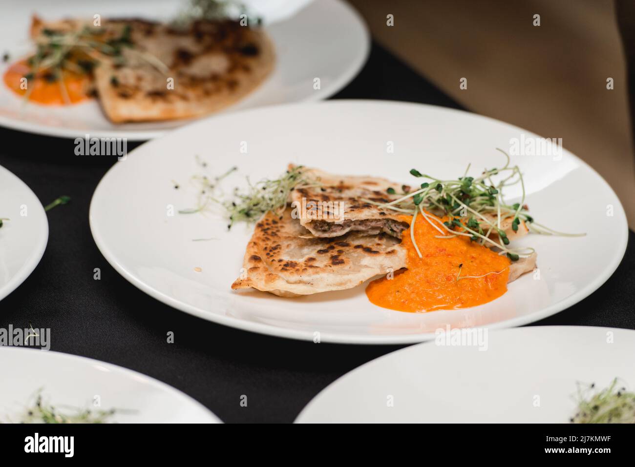 Torta tradizionale di pasta di carne balcanica Cheburek con erbe su un piatto bianco. Servito con salsa e micro verde Foto Stock