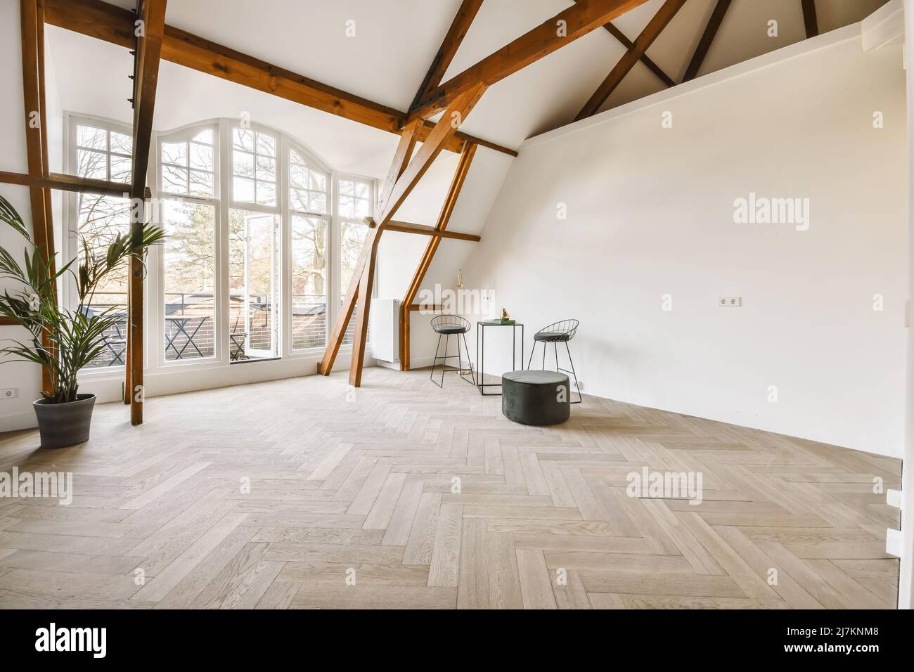 Piccolo tavolo quadrato con sedie e pouf posto in una spaziosa stanza con pavimento in legno e travi decorate con piante in vaso in luce naturale Foto Stock