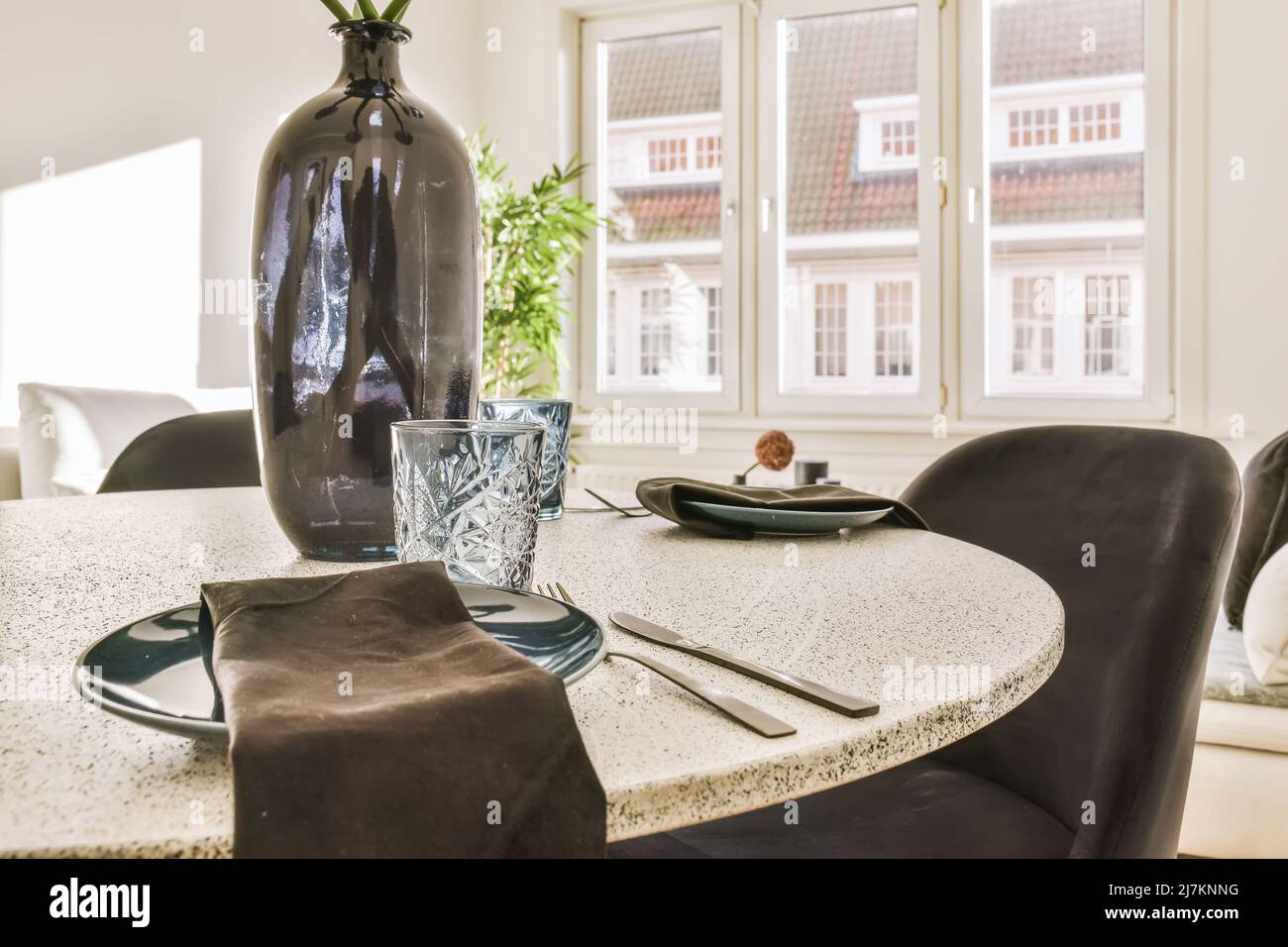 Sedie a tavola con vaso e stoviglie poste vicino a finestre di vetro in una sala da pranzo elegante e luminosa a casa Foto Stock