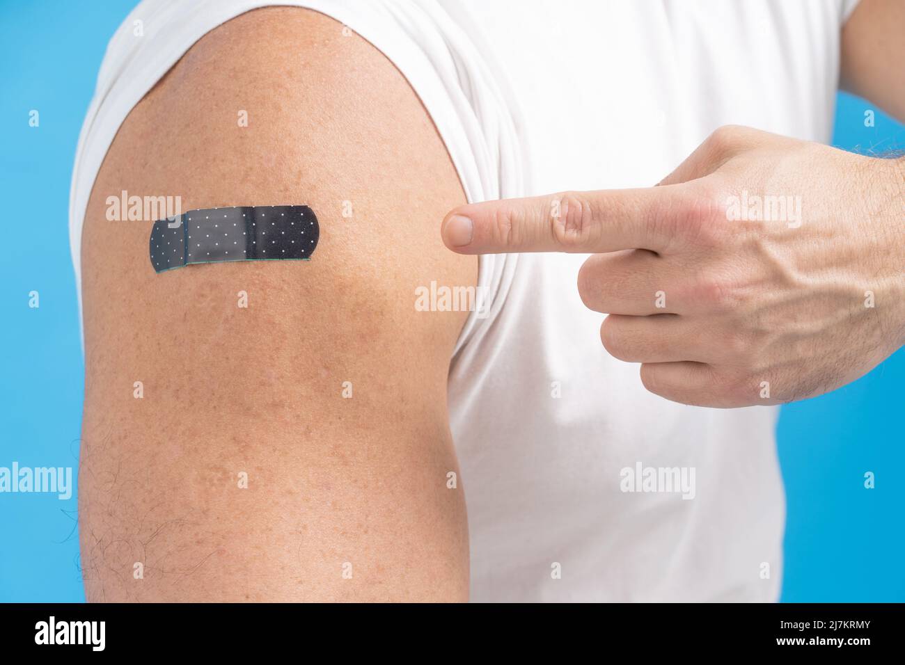 Primo piano un uomo che punta il dito sulla spalla con un aiuto di banda su di esso dopo aver ricevuto il vaccino Covid-19. Vaccino contro COVID-19 o coronavirus. Invecchiamento della pelle maschile. Pelle giusta uomini. Concetto di assistenza sanitaria. Foto Stock