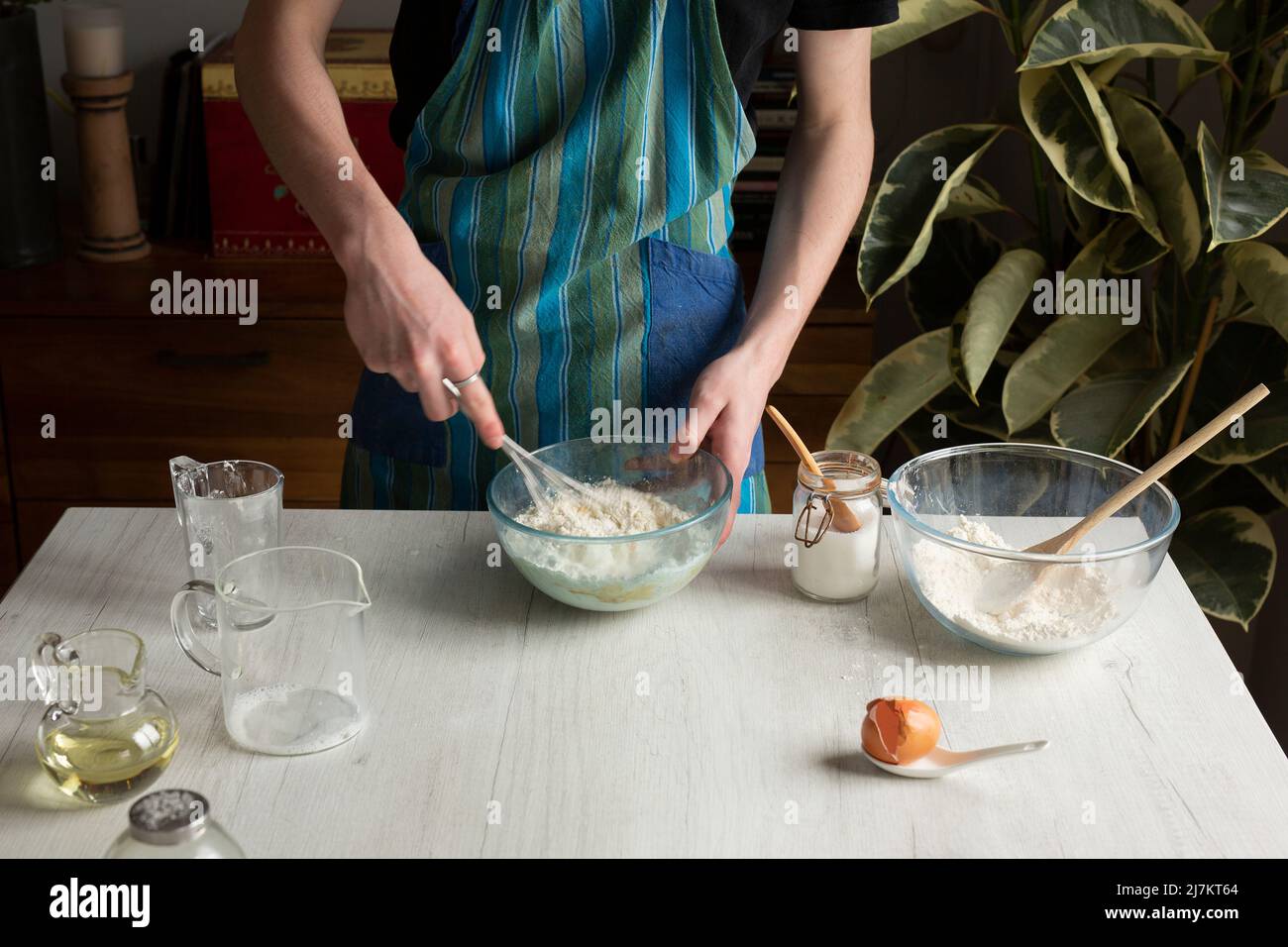 Coltivare persona anonima in pastella di frusta al grembiule per frittelle fatte in casa mentre si cuoce al tavolo con utensili assortiti in cucina leggera Foto Stock