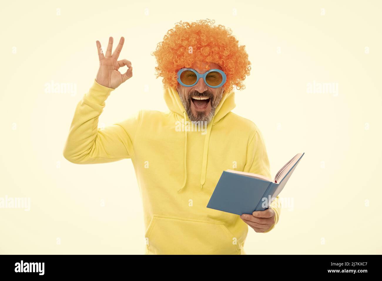Uomo felice in funky show wig OK segno gesto lettura libro scuola in geek occhiali da sole, educazione Foto Stock