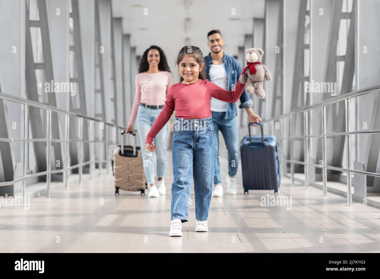 Ritratto di gioiosa ragazza mediorientale carino a piedi in aeroporto con i genitori Foto Stock