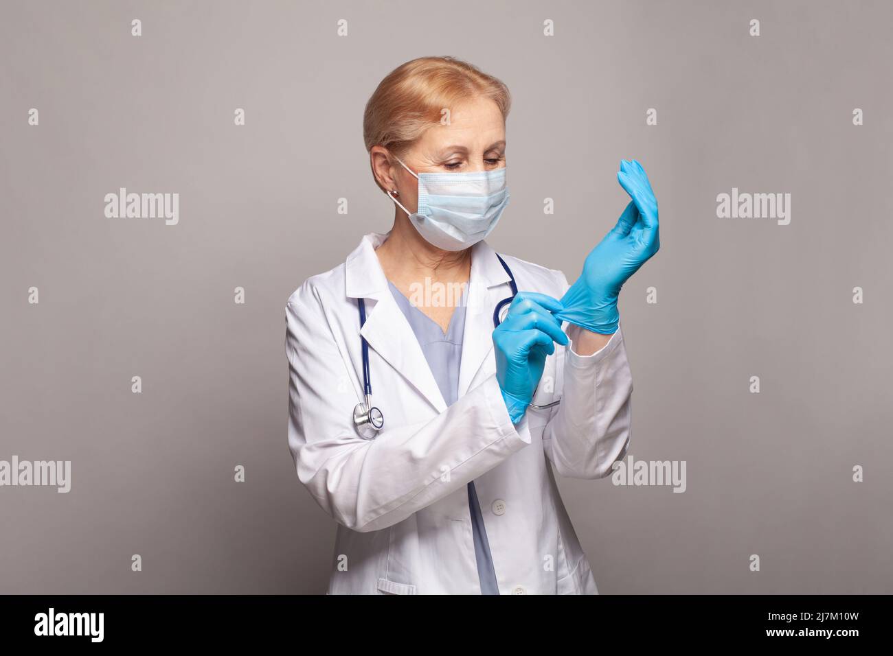 Concetto medico di medico maturo in camice bianco con stetoscopio che mette su guanti medici Foto Stock
