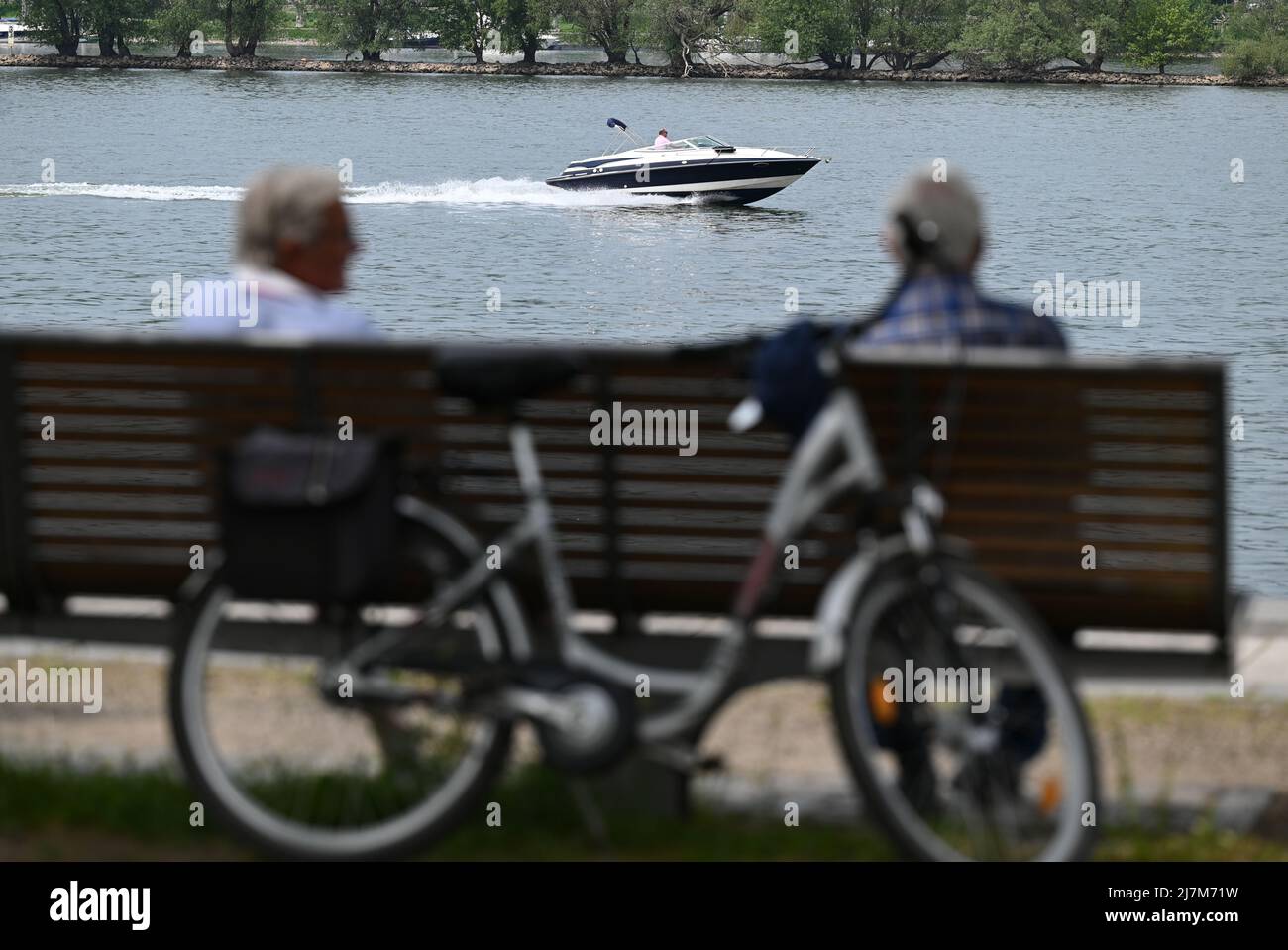 Ingelheim, Germania. 10th maggio 2022. Mentre due uomini siedono su una panchina al traghetto Ingelheim, un motoscafo passa sul Reno. Credit: Arne Dedert/dpa/Alamy Live News Foto Stock