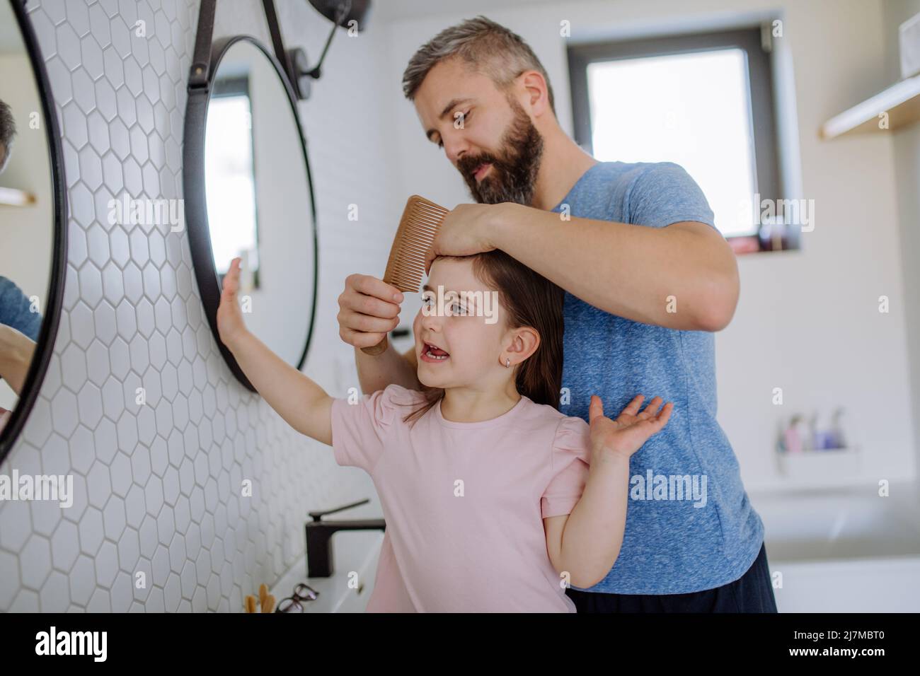 Padre spazzolando i capelli di sua figlia in bagno, mattina concetto di routine. Foto Stock