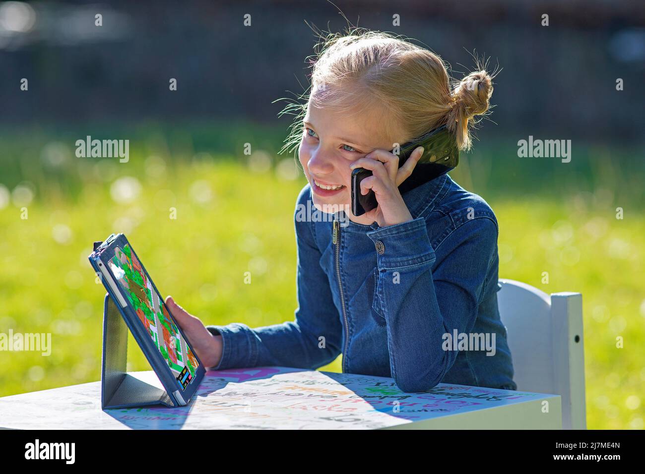 La ragazza con un i-pad, telefono mobile seduto al sole riceve un lotto di radiazioni in questo modo, da tutte le 3 fonti. In fisica, i raggi elettromagnetici Foto Stock