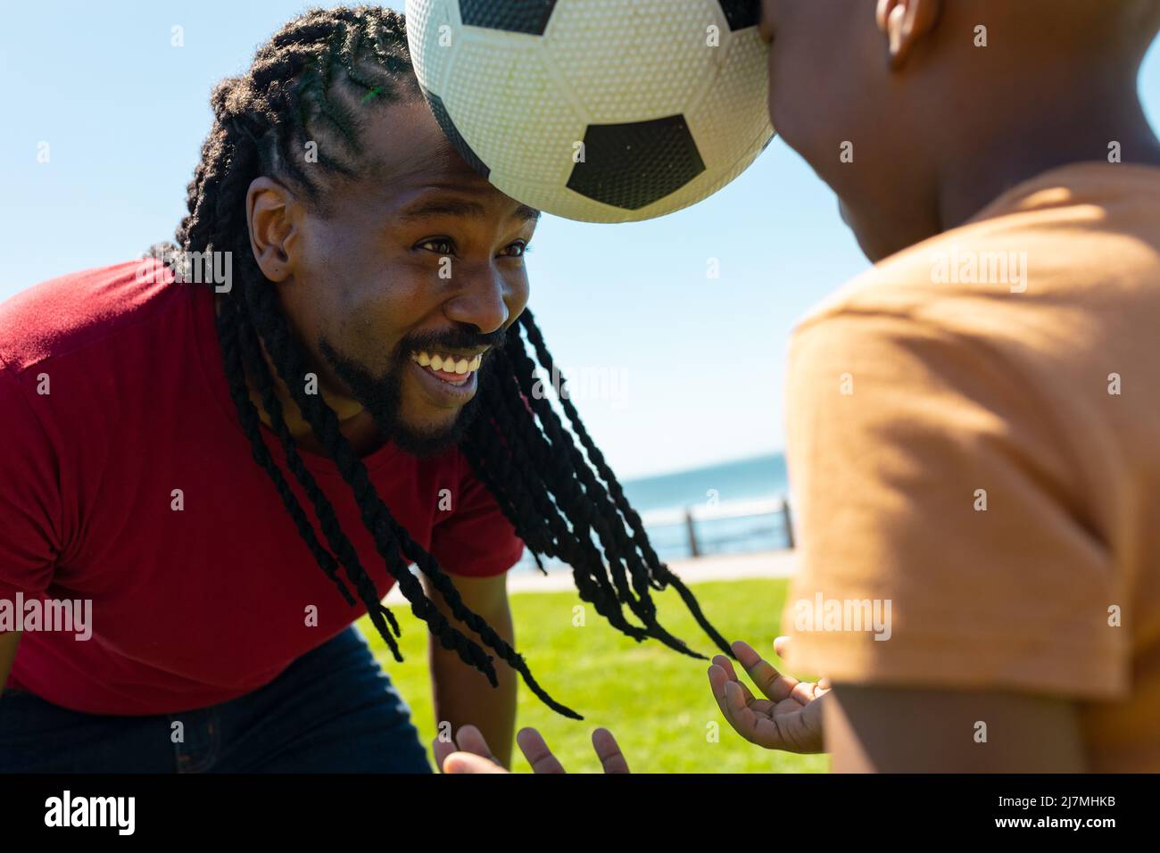 Felice padre e figlio afroamericano che gioca con la palla di calcio in giornata di sole Foto Stock