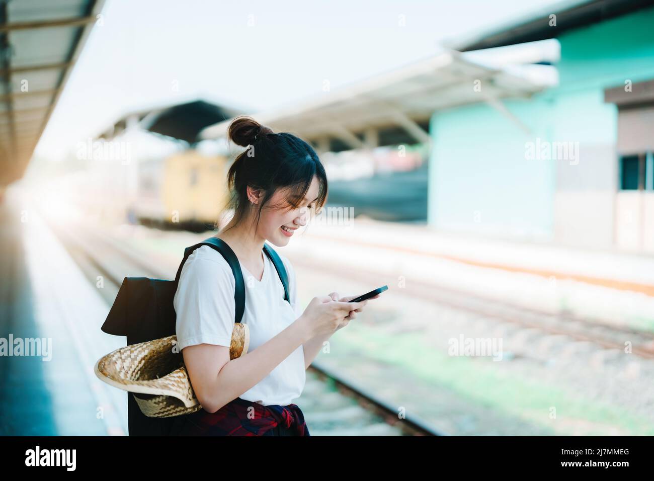 Estate, relax, vacanza, viaggio, ritratto di bella ragazza asiatica utilizzando lo smartphone cellulare per chiamare gli amici alla stazione ferroviaria mentre si aspetta Foto Stock