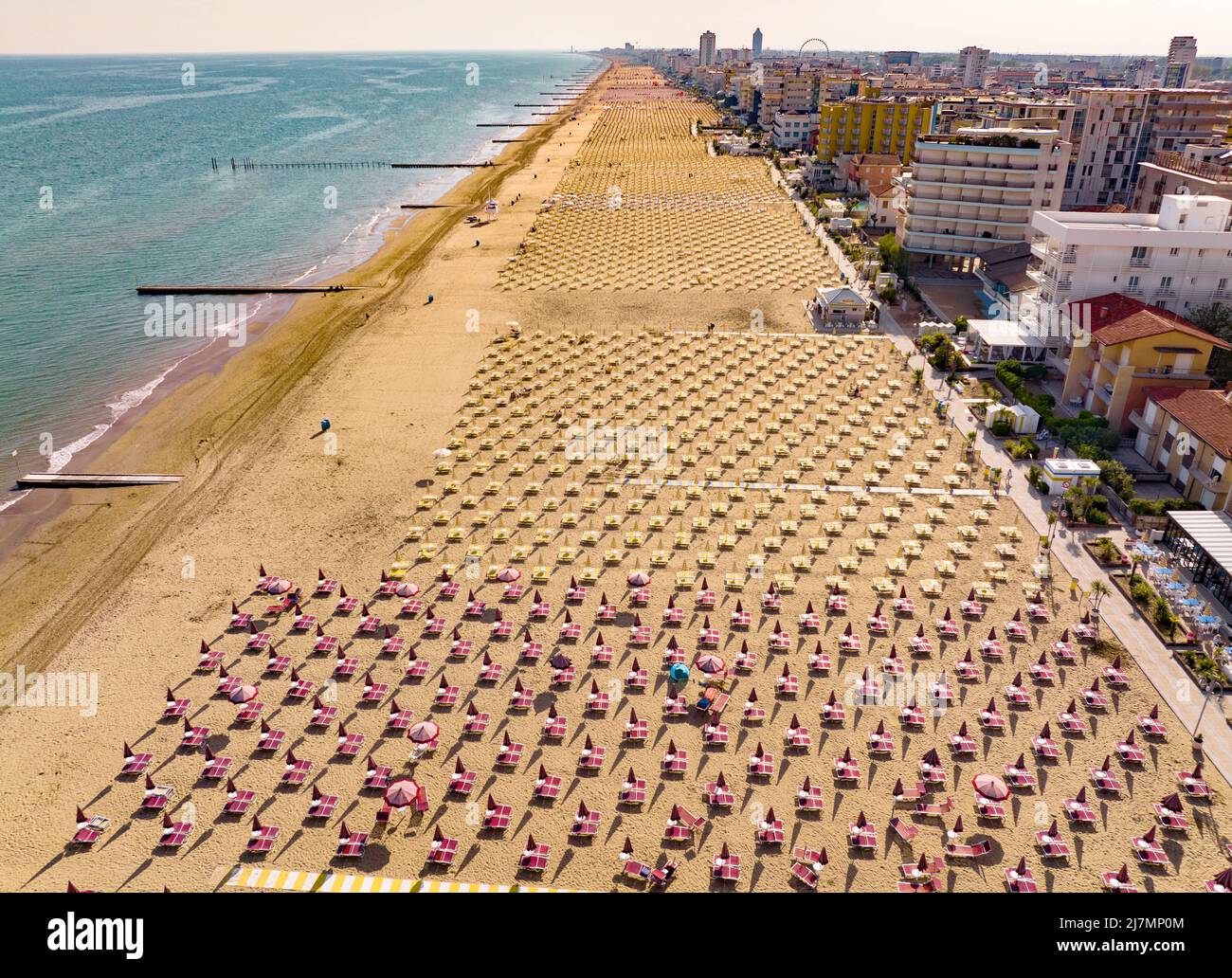 Spiaggia dorata di Jesolo con lettini, sdraio e ombrelloni nella città italiana vista dall'alto durante una giornata di sole con mare calmo Foto Stock