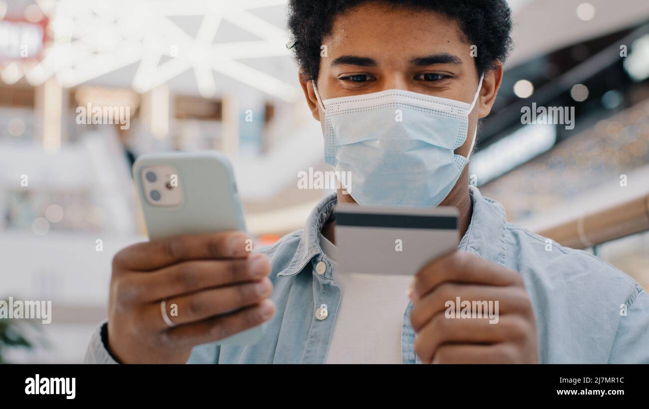 African american man cliente in maschera medica inserimento dati bancari carta di credito in telefono mobile app paga acquistare beni servizi online Foto Stock