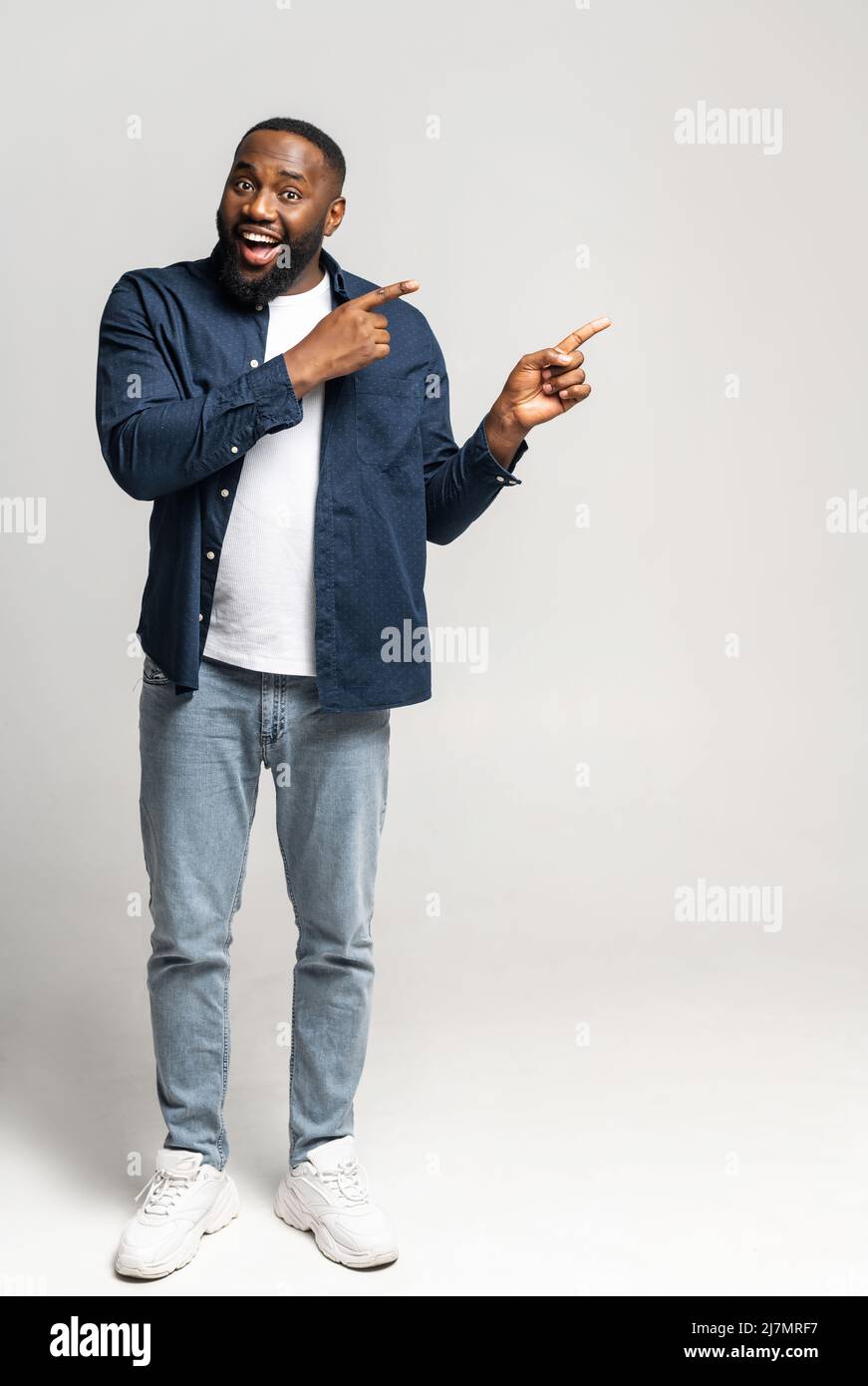 Scatto verticale a tutta lunghezza del ragazzo felice afro-americano eccitato che indossa elegante maglia casual punti dito da parte, spazio vuoto copia per la pubblicità di testo, isolato su grigio Foto Stock