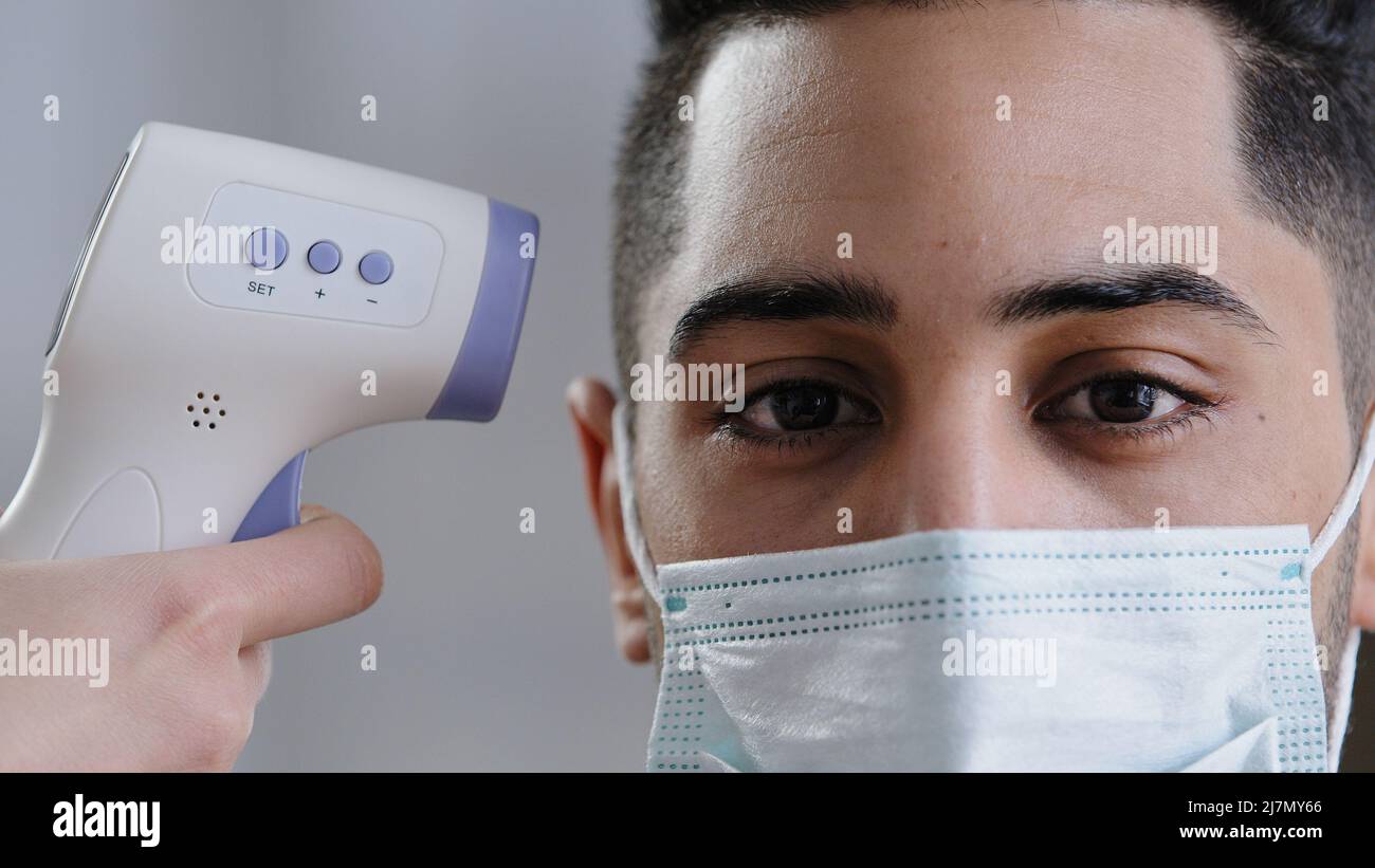 Primo piano-up Visualizza scanner a infrarossi sulla fronte del cliente maschio uomo arabo in maschera medica di protezione scansione temperatura corporea paziente misurazione febbre da Foto Stock